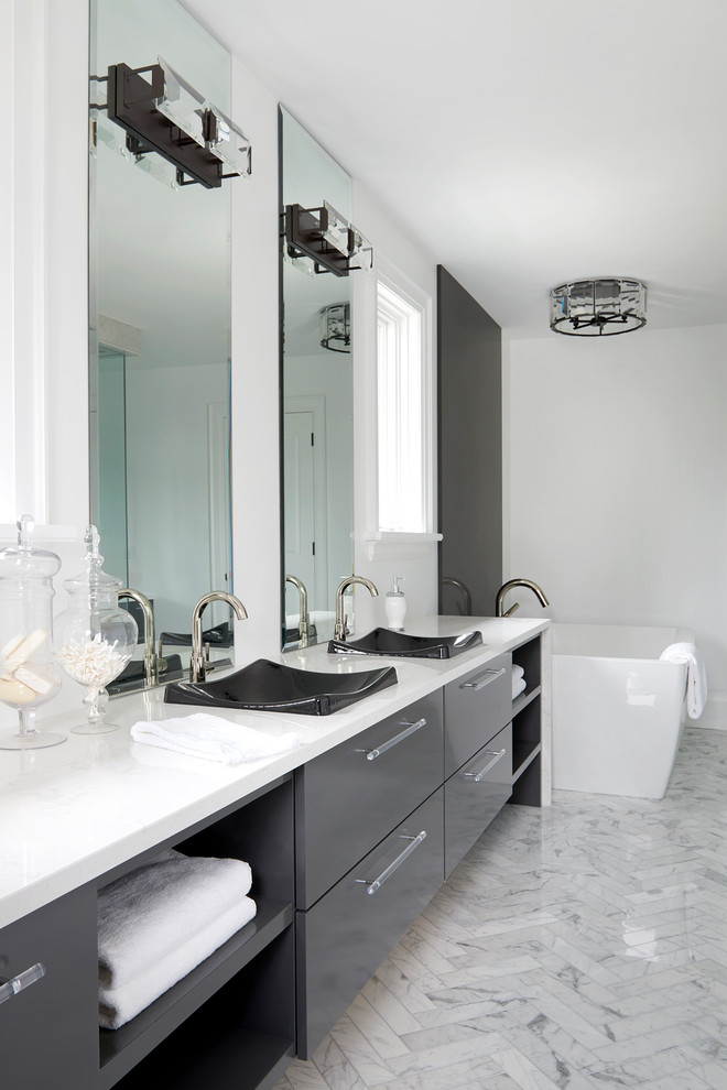 Exemple d'une grande salle de bain principale tendance avec un placard à porte plane, des portes de placard grises, une baignoire indépendante, un carrelage blanc, du carrelage en marbre, un mur blanc, un sol en marbre, une vasque et un plan de toilette en quartz modifié.