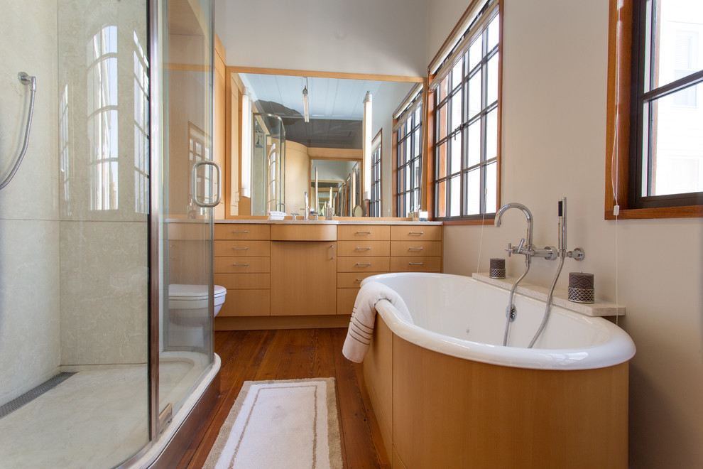 Photo of a medium sized modern ensuite bathroom in Charleston with a submerged sink, flat-panel cabinets, light wood cabinets, marble worktops, a freestanding bath, a walk-in shower, a two-piece toilet, grey walls and medium hardwood flooring.