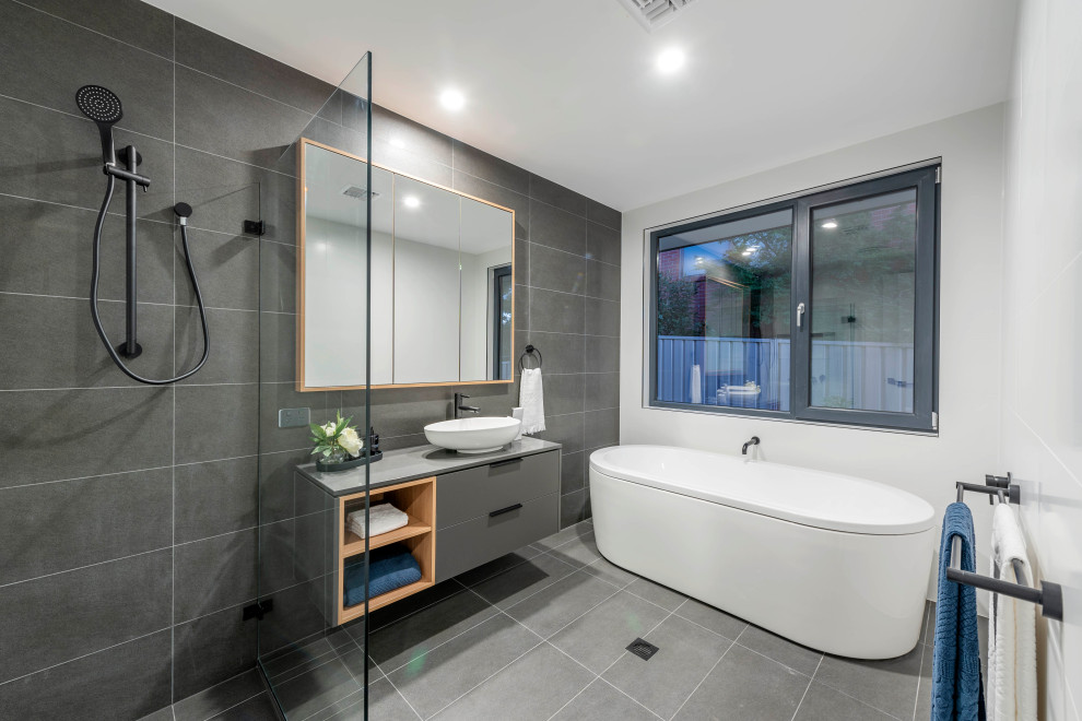 Foto på ett mellanstort funkis grå badrum med dusch, med släta luckor, grå skåp, ett fristående badkar, en öppen dusch, grå kakel, cementkakel, vita väggar, cementgolv, ett konsol handfat, bänkskiva i kvarts, grått golv och med dusch som är öppen