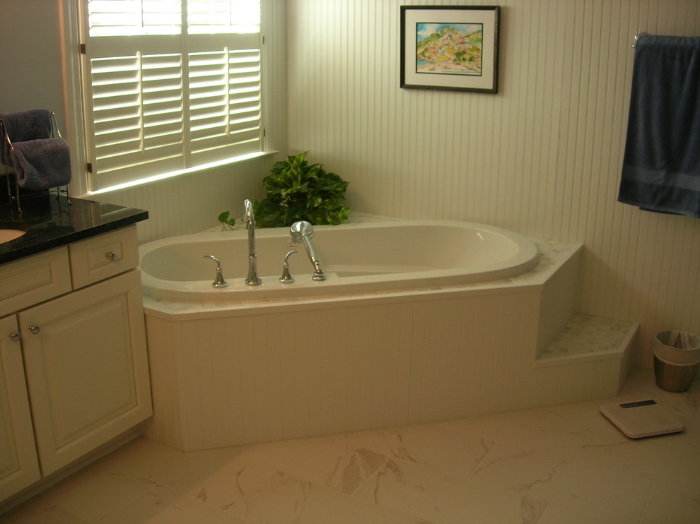 На фото: большая главная ванная комната в стиле неоклассика (современная классика) с фасадами с выступающей филенкой, белыми фасадами, угловой ванной, белыми стенами, врезной раковиной, столешницей из искусственного кварца и белым полом