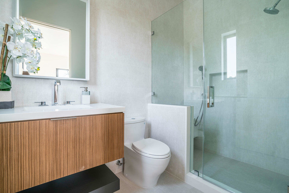Пример оригинального дизайна: ванная комната среднего размера в современном стиле с плоскими фасадами, светлыми деревянными фасадами, душем в нише, унитазом-моноблоком, бежевой плиткой, керамогранитной плиткой, бежевыми стенами, бетонным полом, душевой кабиной, врезной раковиной, столешницей из искусственного камня, бежевым полом и душем с распашными дверями