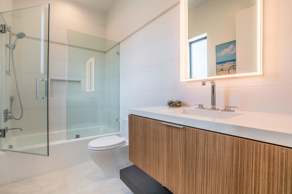 Medium sized contemporary shower room bathroom in Los Angeles with flat-panel cabinets, light wood cabinets, an alcove bath, a shower/bath combination, a one-piece toilet, white tiles, ceramic tiles, white walls, ceramic flooring, an integrated sink, solid surface worktops, white floors and a hinged door.