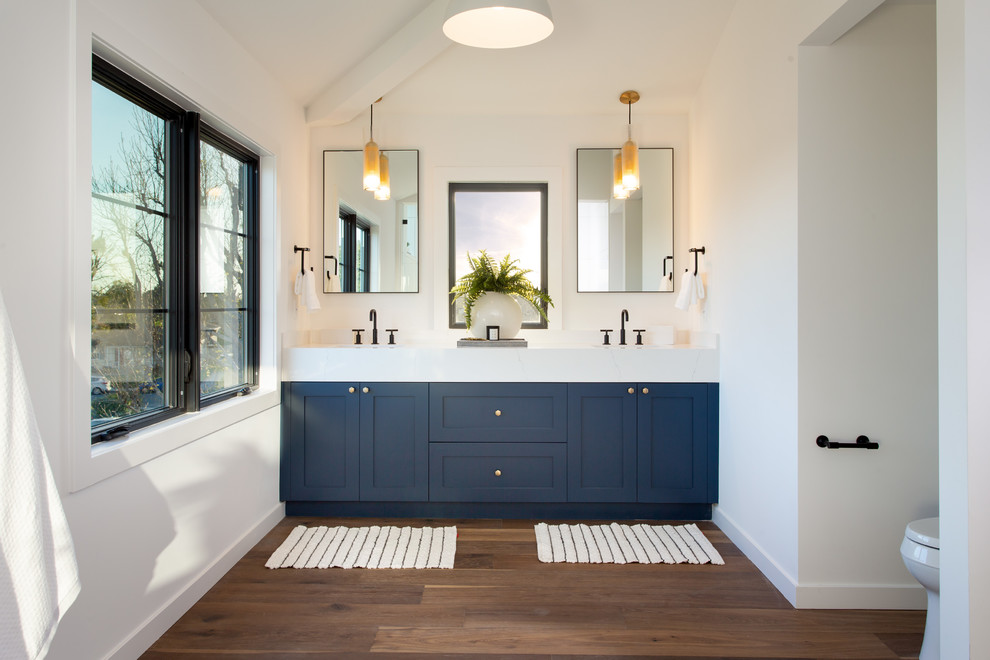 Klassisches Badezimmer mit Schrankfronten im Shaker-Stil, blauen Schränken, weißer Wandfarbe, dunklem Holzboden, braunem Boden und weißer Waschtischplatte in Los Angeles