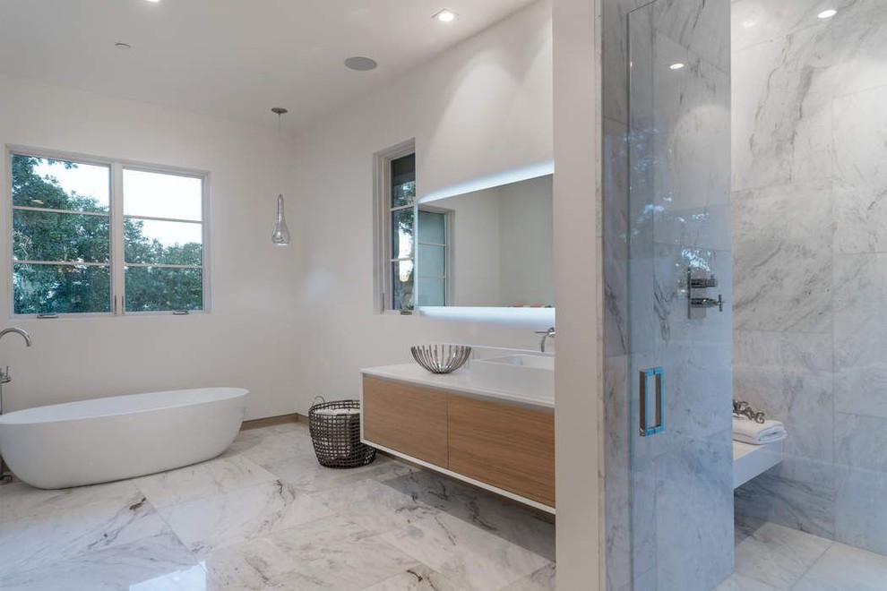 Exemple d'une grande douche en alcôve principale tendance en bois clair avec un placard à porte plane, une baignoire indépendante, un carrelage gris, du carrelage en marbre, un mur blanc, un sol en marbre, une vasque, un plan de toilette en surface solide, un sol blanc, une cabine de douche à porte battante et un plan de toilette blanc.