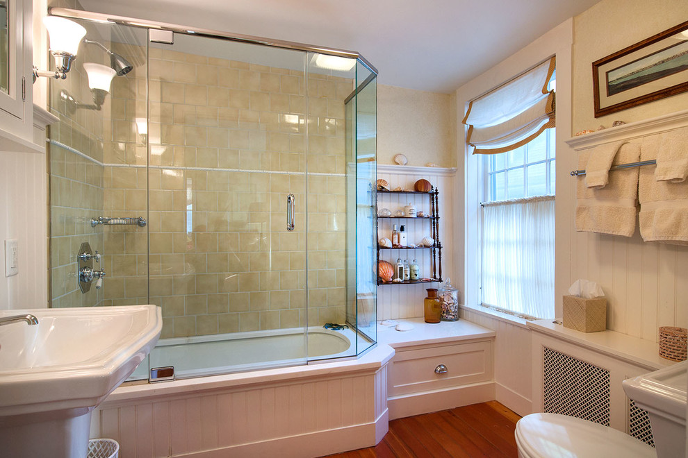 Inspiration for a mid-sized coastal 3/4 beige tile and ceramic tile medium tone wood floor tub/shower combo remodel in New York with beaded inset cabinets, white cabinets, an undermount tub, a one-piece toilet, beige walls, a pedestal sink and solid surface countertops