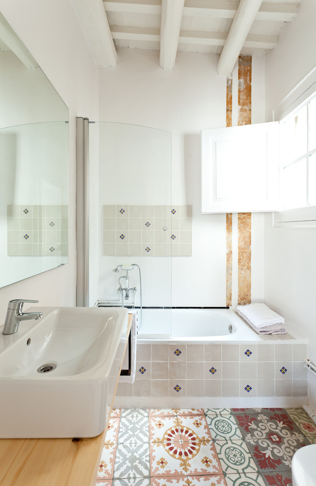 Aménagement d'une salle de bain principale éclectique de taille moyenne avec un carrelage multicolore, des carreaux de céramique, un combiné douche/baignoire, une vasque, un mur blanc, une baignoire en alcôve, un sol en carrelage de céramique, un plan de toilette en bois et une fenêtre.