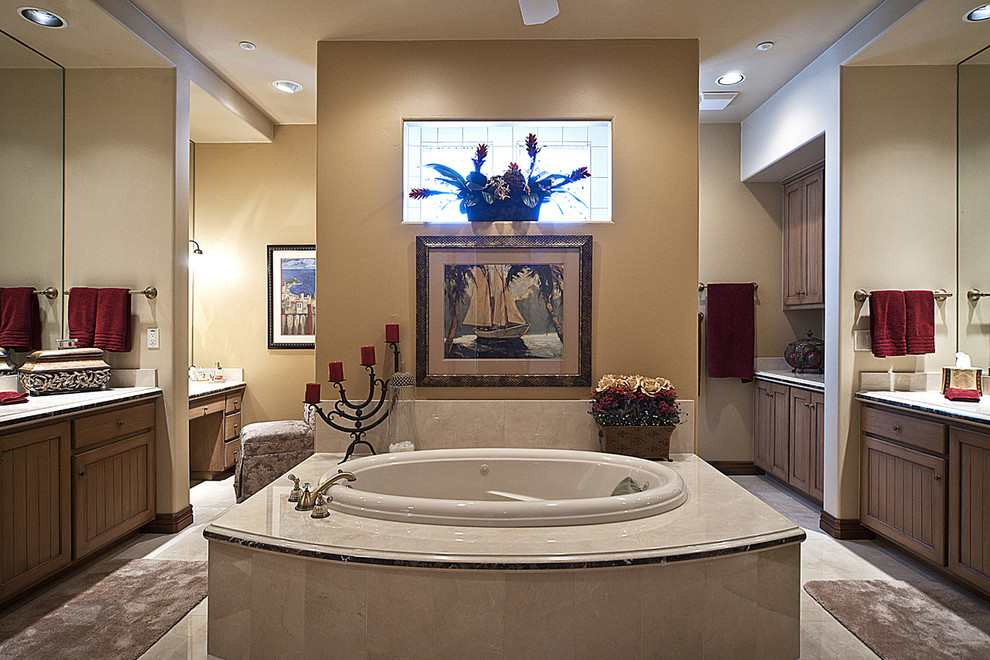 Example of a tuscan beige tile drop-in bathtub design in Phoenix with recessed-panel cabinets and medium tone wood cabinets