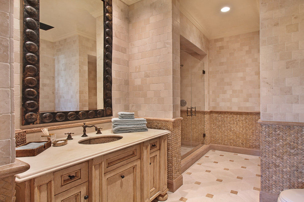 Immagine di una stanza da bagno mediterranea con lavabo sottopiano, ante in legno chiaro, doccia alcova, piastrelle beige, piastrelle in pietra e ante con riquadro incassato