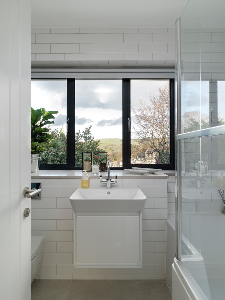 Cette photo montre une petite salle de bain principale tendance avec une baignoire posée, un combiné douche/baignoire, WC suspendus, un carrelage gris, des carreaux de céramique, un mur blanc, un lavabo suspendu, un sol gris et aucune cabine.