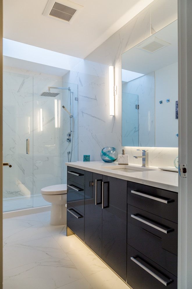 Modern inredning av ett mellanstort en-suite badrum, med släta luckor, grå skåp, en dusch i en alkov, en toalettstol med hel cisternkåpa, vit kakel, porslinskakel, vita väggar, klinkergolv i porslin, ett undermonterad handfat och bänkskiva i kvarts