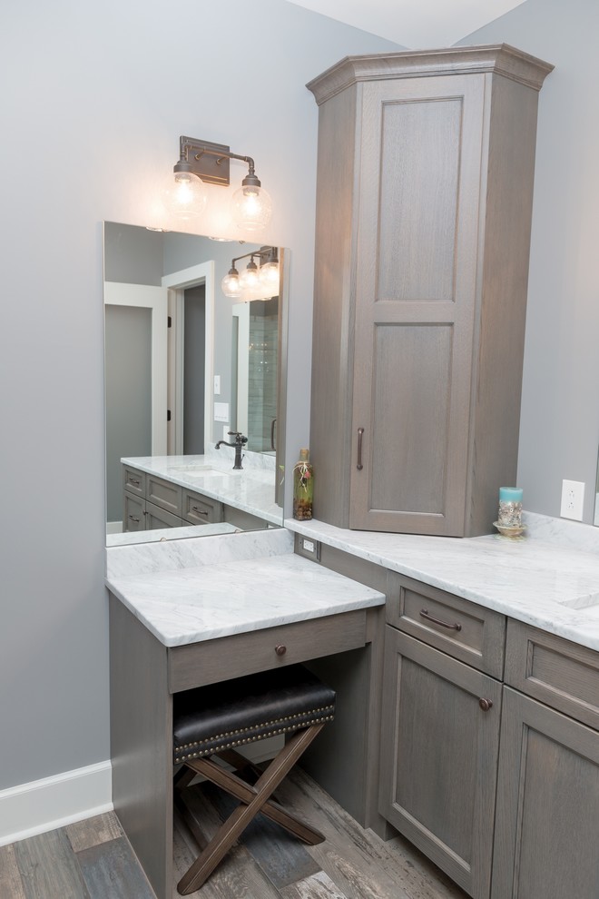 Cette photo montre une salle de bain principale chic de taille moyenne avec un placard à porte shaker, des portes de placard grises, un mur gris, un lavabo encastré, un plan de toilette en marbre, un sol marron et un plan de toilette blanc.