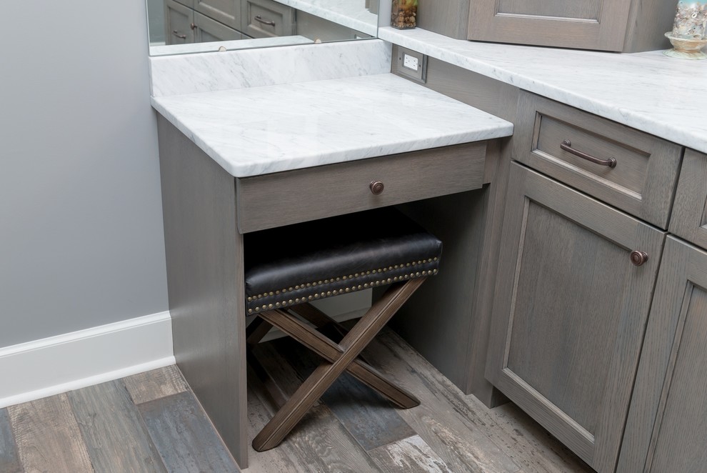 Cette image montre une salle de bain principale traditionnelle de taille moyenne avec un placard à porte shaker, des portes de placard grises, un mur gris, un lavabo encastré, un plan de toilette en marbre, un sol marron et un plan de toilette blanc.