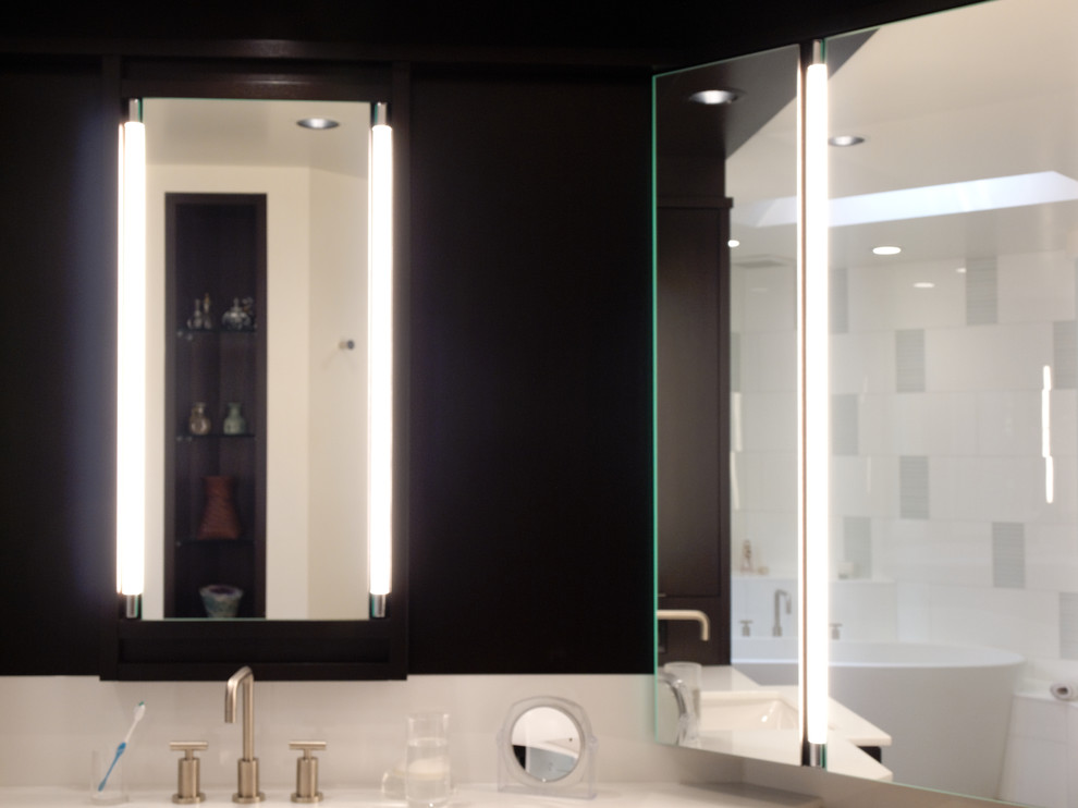 На фото: большая главная ванная комната в современном стиле с плоскими фасадами, коричневыми фасадами, отдельно стоящей ванной, раздельным унитазом, стеклянной плиткой, белыми стенами, полом из известняка, врезной раковиной и мраморной столешницей с