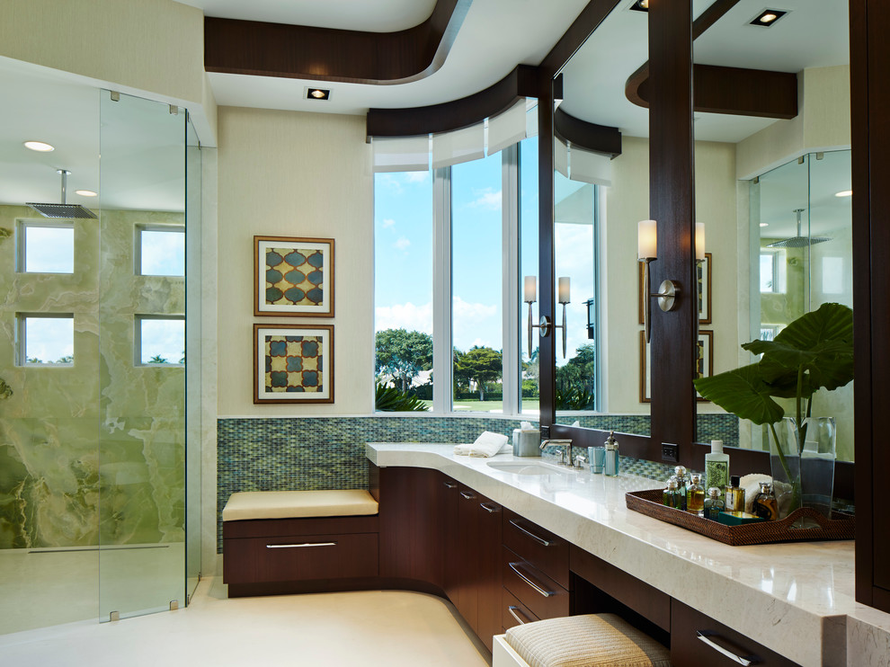 This is an example of an expansive contemporary ensuite bathroom in Miami with a submerged sink, flat-panel cabinets, dark wood cabinets, limestone worktops, a built-in shower, blue tiles, glass tiles, beige walls and porcelain flooring.