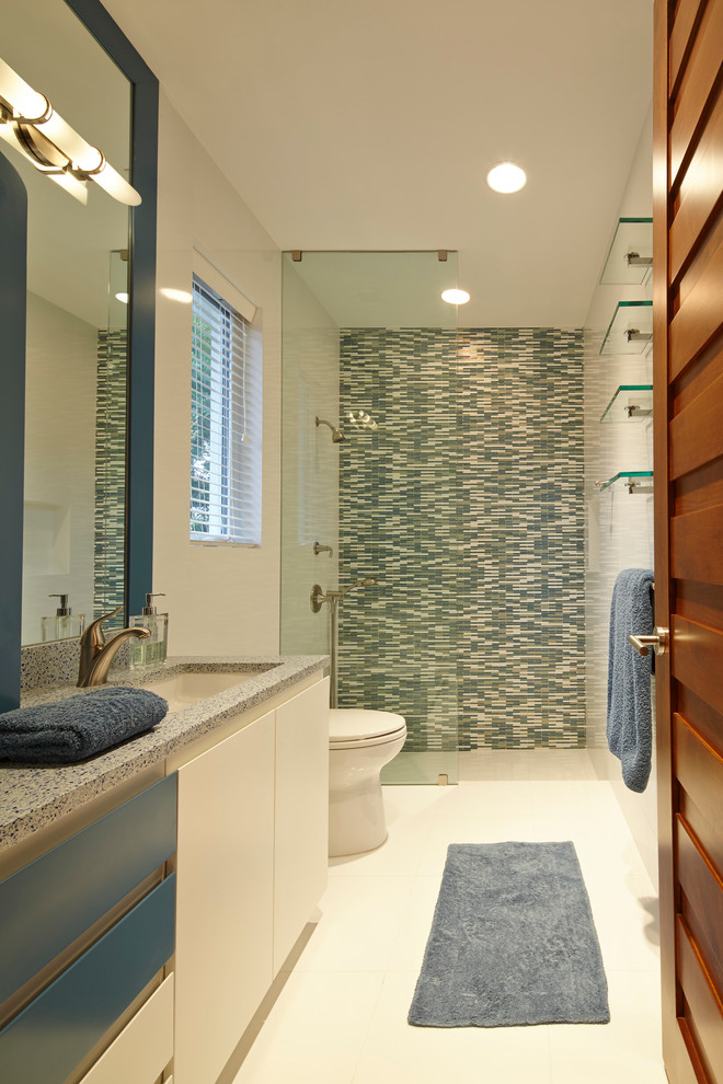 Bild på ett stort funkis badrum, med ett undermonterad handfat, släta luckor, blå skåp, bänkskiva i terrazo, en kantlös dusch, en toalettstol med hel cisternkåpa, blå kakel, stickkakel, vita väggar och klinkergolv i porslin