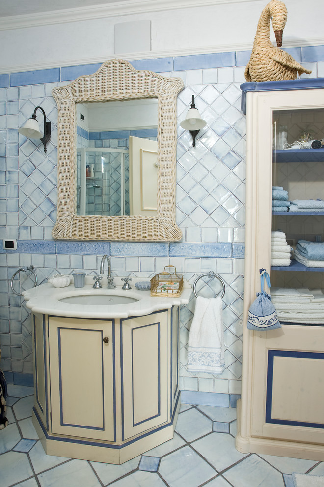 Ispirazione per una stanza da bagno mediterranea con ante con riquadro incassato, ante in legno chiaro, piastrelle blu, piastrelle in ceramica, pavimento con piastrelle in ceramica, lavabo integrato e top in marmo