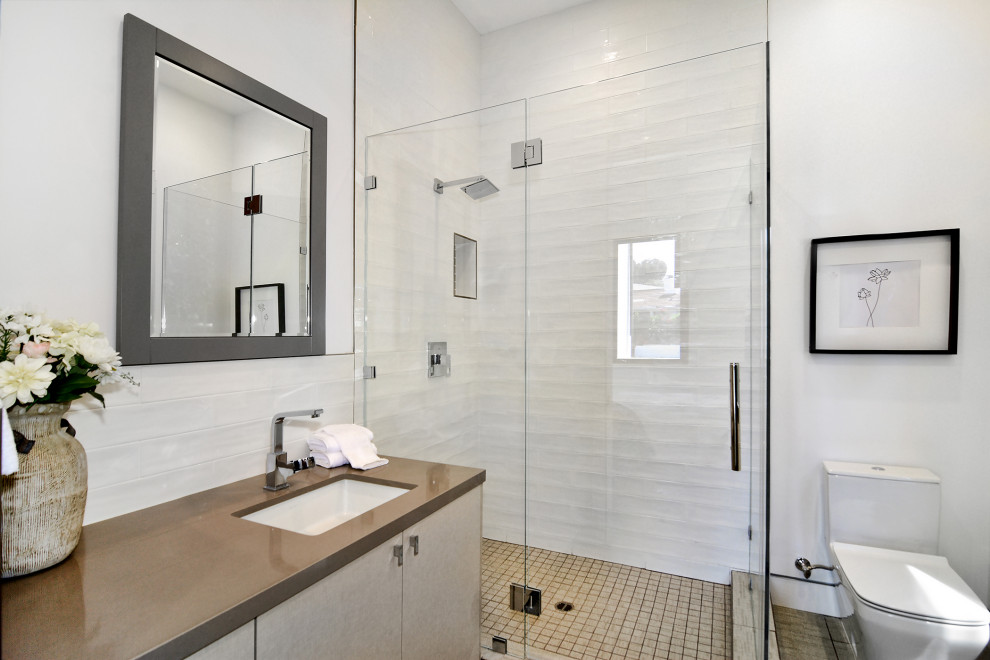 На фото: ванная комната среднего размера в стиле модернизм с плоскими фасадами, светлыми деревянными фасадами, угловым душем, унитазом-моноблоком, белой плиткой, цементной плиткой, белыми стенами, полом из цементной плитки, врезной раковиной, столешницей из искусственного кварца, бежевым полом, душем с распашными дверями, коричневой столешницей, нишей и тумбой под одну раковину