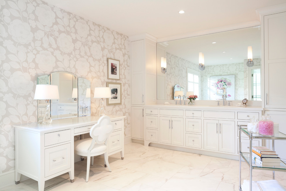 Aménagement d'une grande salle de bain principale classique avec des portes de placard blanches, une baignoire indépendante, un mur beige, un sol en marbre, meuble double vasque, du papier peint, meuble-lavabo encastré et un placard avec porte à panneau encastré.