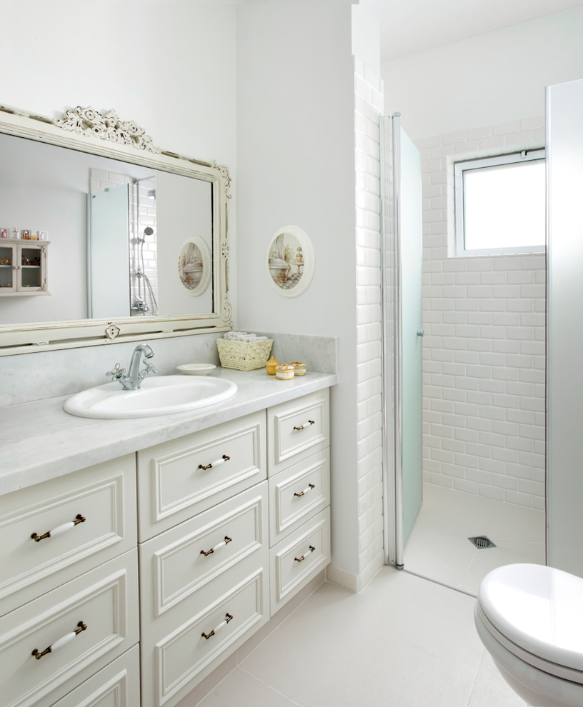 На фото: ванная комната в классическом стиле с фасадами с утопленной филенкой, белыми фасадами, душем без бортиков, белой плиткой, плиткой кабанчик, белыми стенами и белой столешницей с