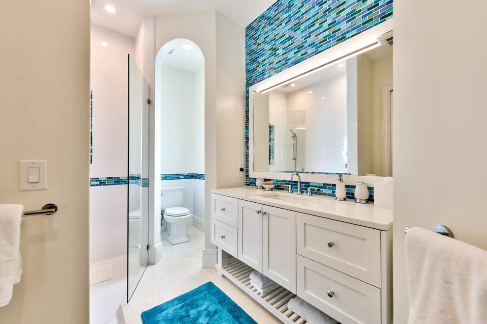 Пример оригинального дизайна: главная ванная комната среднего размера в морском стиле с белыми фасадами, столешницей из искусственного кварца, душем без бортиков, раздельным унитазом, синей плиткой, удлиненной плиткой, бежевыми стенами, врезной раковиной, фасадами в стиле шейкер, полом из керамической плитки, бежевым полом, душем с распашными дверями и белой столешницей