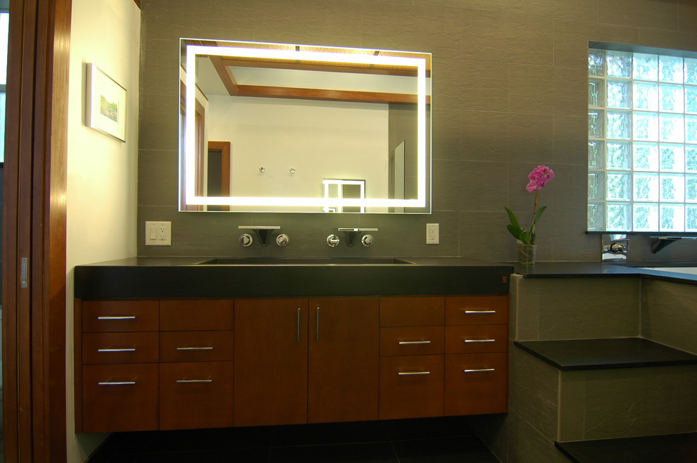 Идея дизайна: ванная комната в восточном стиле с раковиной с несколькими смесителями, плоскими фасадами, фасадами цвета дерева среднего тона, полновстраиваемой ванной, открытым душем, черной плиткой и каменной плиткой
