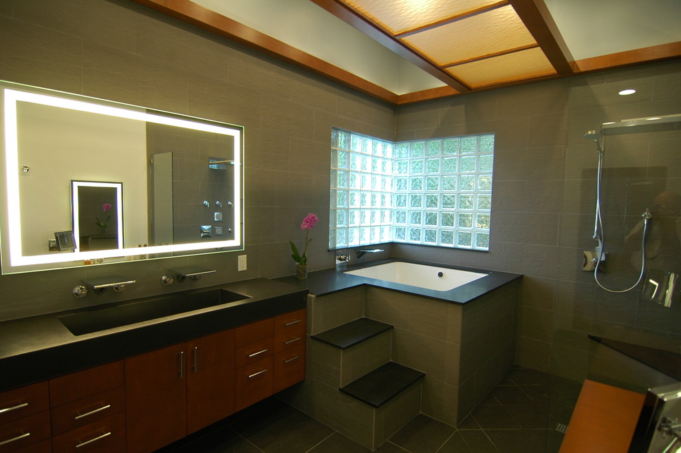 Foto di una stanza da bagno etnica con lavabo rettangolare, ante lisce, ante in legno scuro, vasca sottopiano, doccia aperta, piastrelle nere e piastrelle in pietra