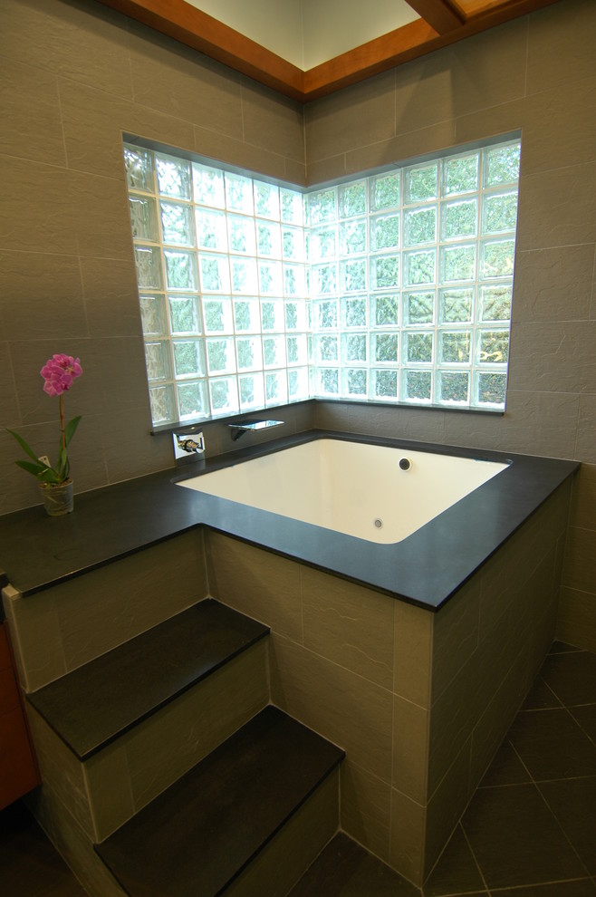 Asiatisk inredning av ett badrum, med ett undermonterat badkar, en öppen dusch, svart kakel och stenkakel