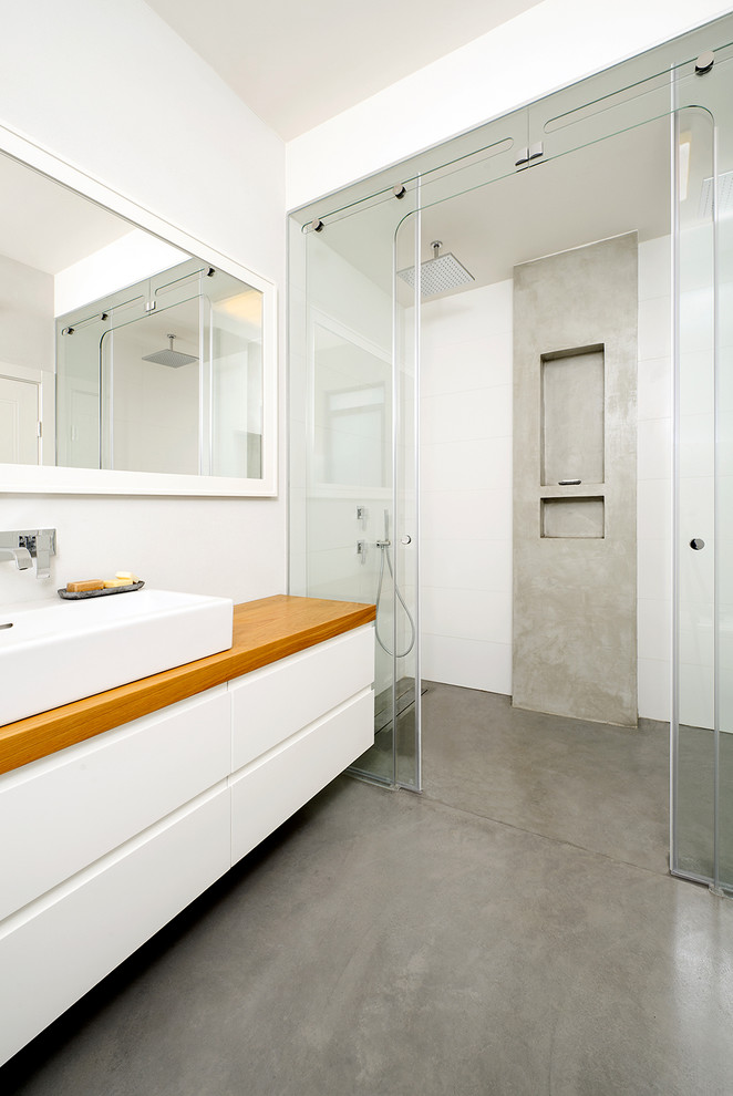 На фото: ванная комната в современном стиле с настольной раковиной, столешницей из дерева и бетонным полом с