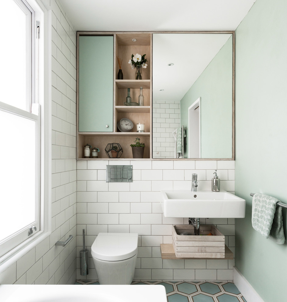 Inredning av ett skandinaviskt badrum, med släta luckor, gröna skåp, en vägghängd toalettstol, vit kakel, tunnelbanekakel, gröna väggar, ett väggmonterat handfat och flerfärgat golv