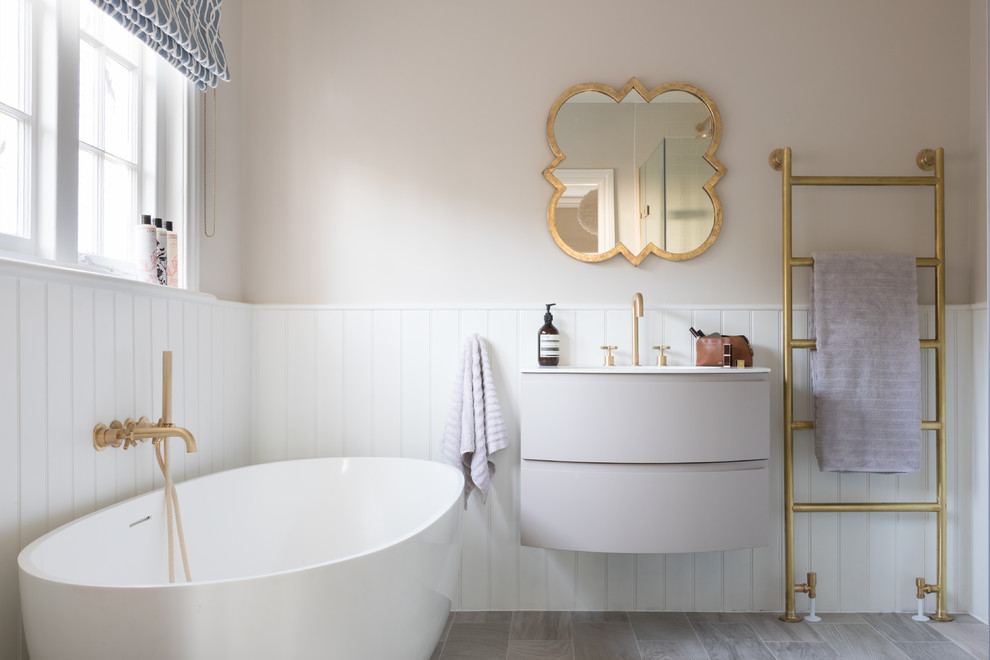 Modelo de cuarto de baño contemporáneo de tamaño medio con bañera exenta, paredes beige, suelo de madera clara, lavabo suspendido, armarios con paneles lisos, suelo gris, encimeras blancas y puertas de armario grises