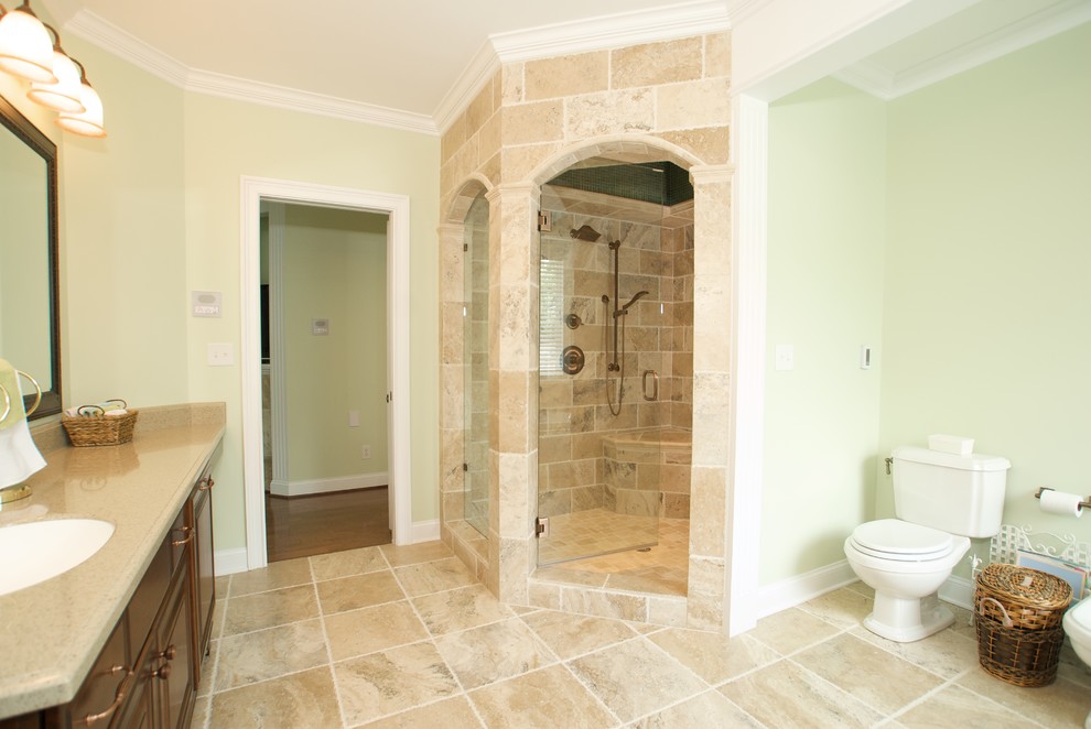 Example of a large classic master beige tile and stone tile travertine floor bathroom design in Other with raised-panel cabinets, dark wood cabinets, a two-piece toilet, green walls, an undermount sink and solid surface countertops