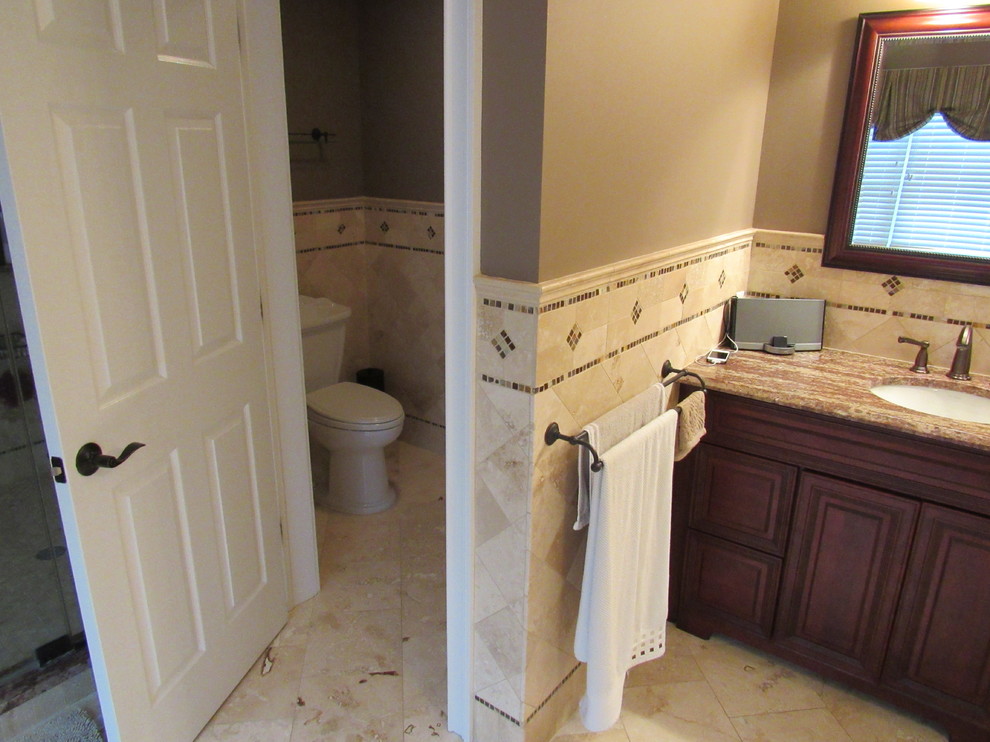 Mid-sized elegant master beige tile, brown tile and porcelain tile travertine floor bathroom photo in New York with raised-panel cabinets, dark wood cabinets, a one-piece toilet, multicolored walls, an undermount sink and granite countertops