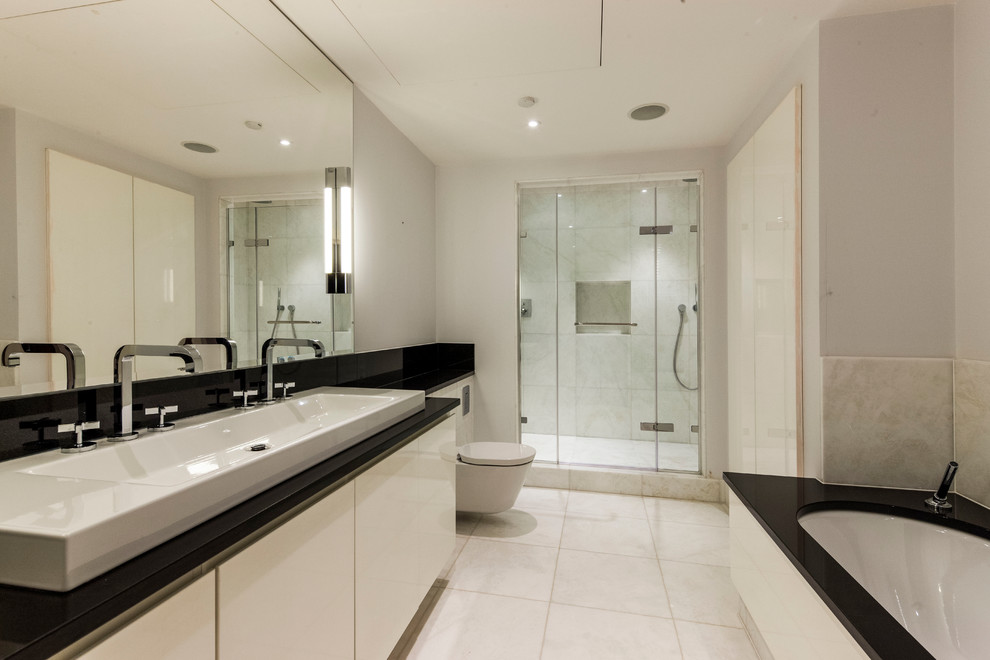 Large modern family bathroom in London with a built-in bath, a walk-in shower, a wall mounted toilet, beige tiles, beige walls, ceramic flooring, a trough sink and marble worktops.