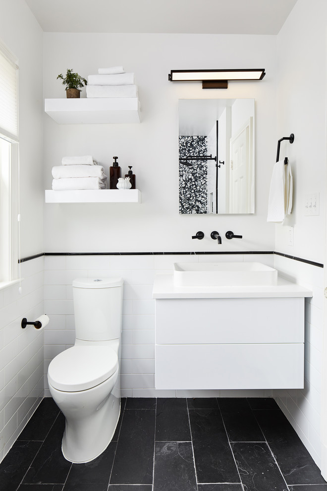 Cette photo montre une petite salle d'eau tendance avec un placard à porte plane, des portes de placard blanches, un carrelage blanc, un mur blanc, une vasque, un sol noir et un plan de toilette blanc.