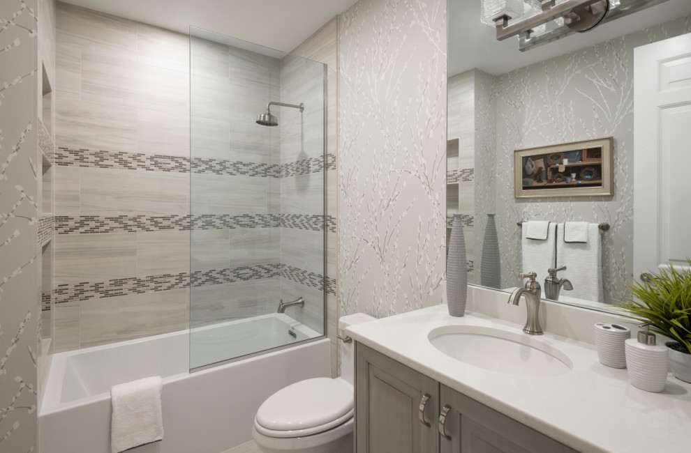 Пример оригинального дизайна: ванная комната среднего размера в стиле неоклассика (современная классика) с фасадами с утопленной филенкой, серыми фасадами, накладной ванной, душем над ванной, унитазом-моноблоком, серой плиткой, плиткой из листового стекла, серыми стенами, полом из керамогранита, душевой кабиной, врезной раковиной, столешницей из кварцита, серым полом, открытым душем, белой столешницей, тумбой под одну раковину, встроенной тумбой и обоями на стенах