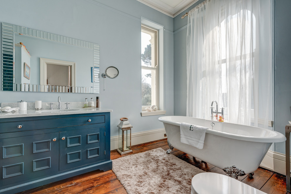 Inspiration pour une grande salle d'eau traditionnelle en bois vieilli avec un placard à porte affleurante, un plan de toilette en marbre, une baignoire sur pieds, WC séparés, un mur bleu et un sol en bois brun.