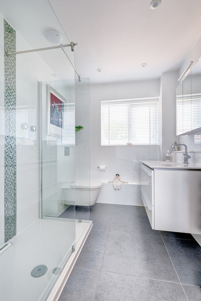 Inspiration för små klassiska en-suite badrum, med ett integrerad handfat, släta luckor, en vägghängd toalettstol, vit kakel, keramikplattor, vita väggar, klinkergolv i keramik, vita skåp och grått golv