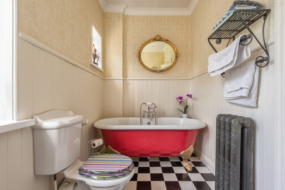 Lantlig inredning av ett badrum, med ett badkar med tassar, en toalettstol med separat cisternkåpa och beige väggar