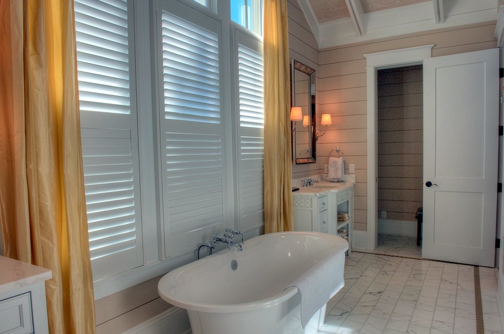 Cette image montre une salle de bain principale marine de taille moyenne avec un lavabo encastré, un placard en trompe-l'oeil, des portes de placard blanches, un plan de toilette en marbre, une baignoire indépendante, WC à poser, un mur beige et un sol en marbre.