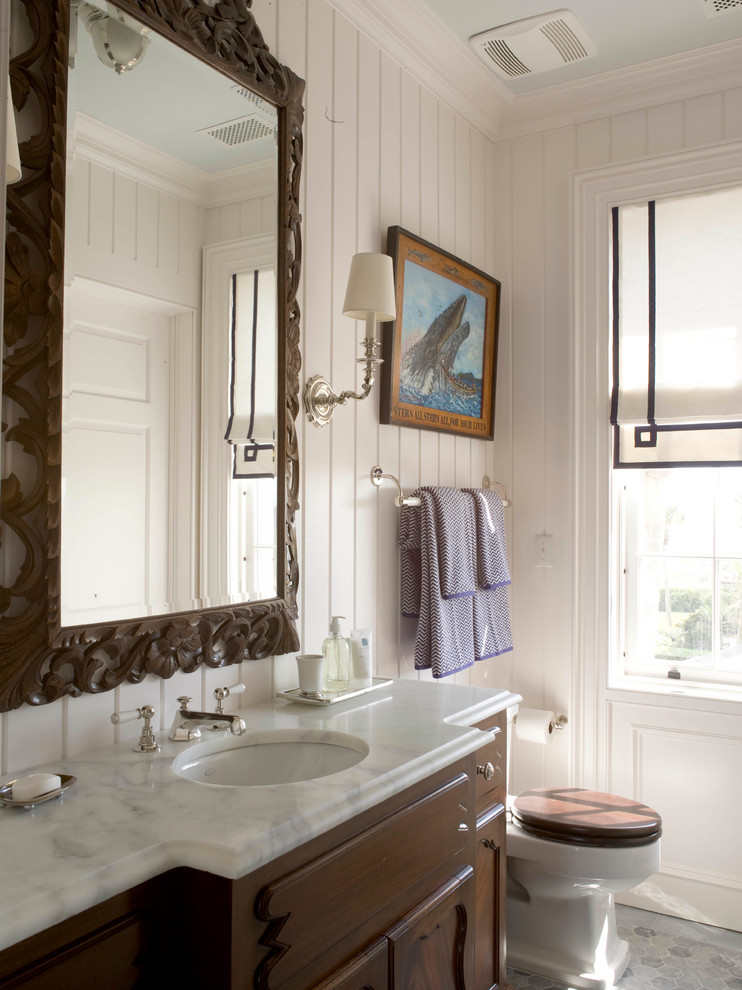 Cette image montre une grande salle de bain marine en bois brun avec WC séparés, un mur blanc, un lavabo encastré et un plan de toilette en marbre.