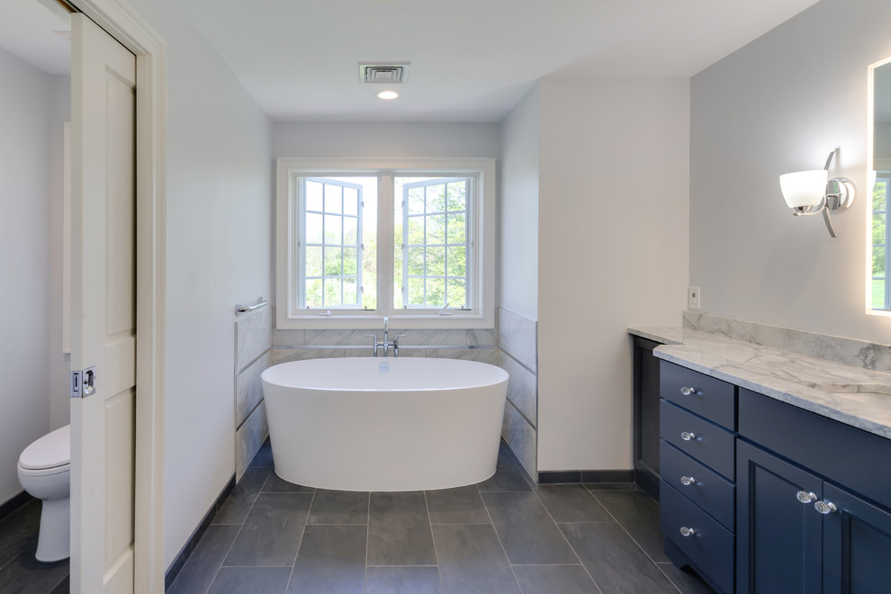Idéer för att renovera ett stort vintage grå grått en-suite badrum, med släta luckor, blå skåp, ett fristående badkar, en öppen dusch, en toalettstol med separat cisternkåpa, grå kakel, porslinskakel, grå väggar, klinkergolv i porslin, ett undermonterad handfat, granitbänkskiva, grått golv och med dusch som är öppen