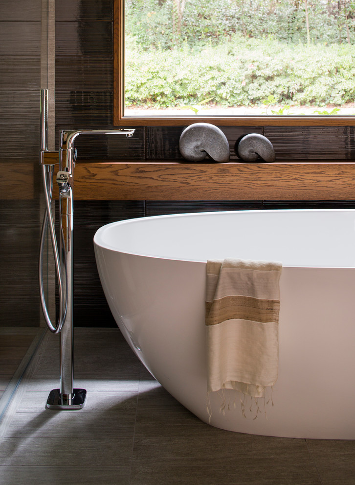 Modern inredning av ett en-suite badrum, med ett fristående handfat, skåp i mellenmörkt trä, bänkskiva i akrylsten, ett fristående badkar, brun kakel och grå väggar