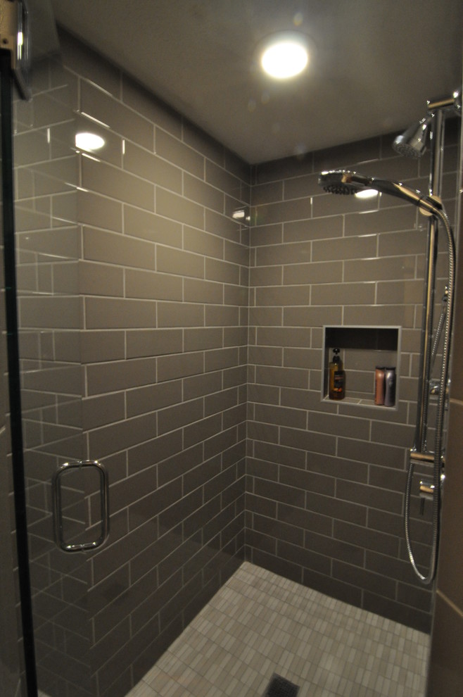 Inredning av ett modernt litet badrum med dusch, med släta luckor, skåp i ljust trä, en hörndusch, en toalettstol med separat cisternkåpa, grå kakel, vita väggar och ett undermonterad handfat