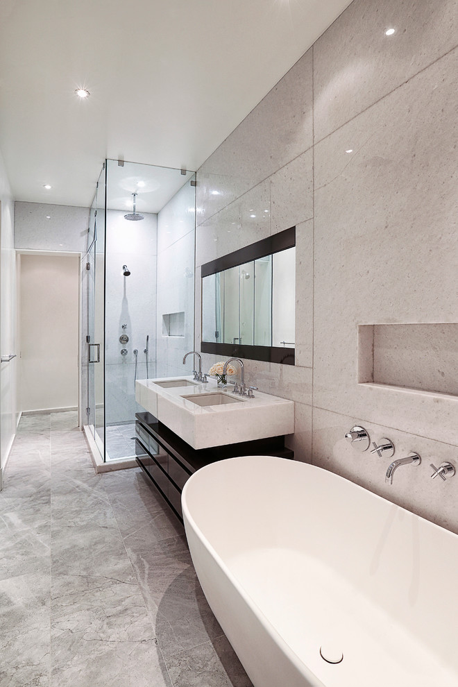 Modern inredning av ett badrum, med släta luckor, ett fristående badkar, en hörndusch, grå kakel och ett undermonterad handfat