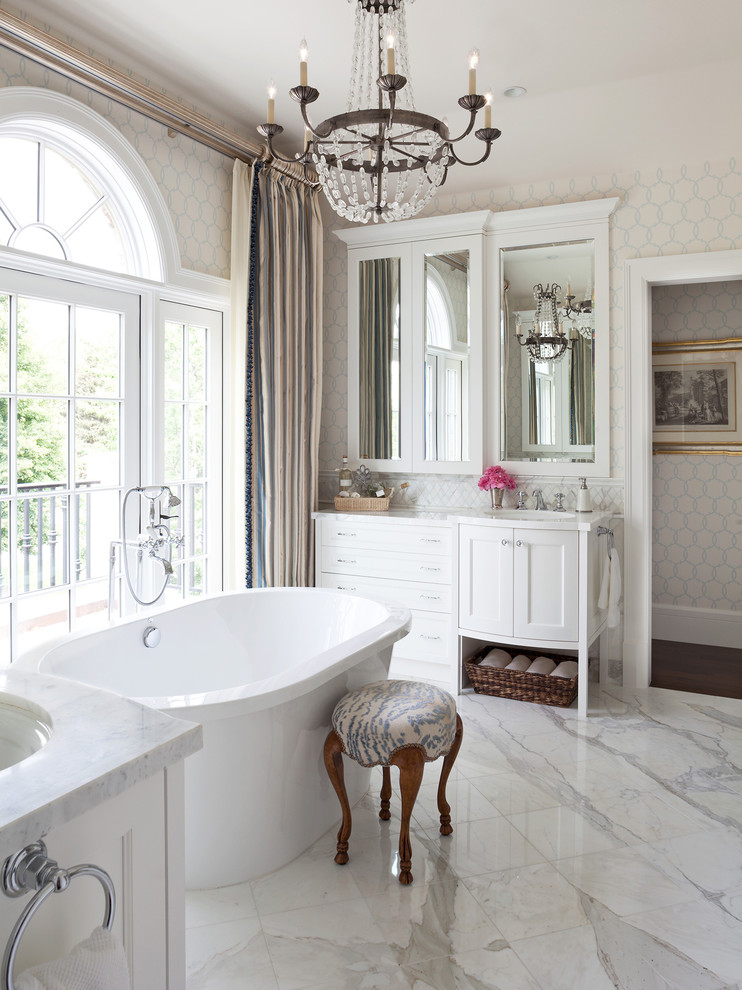 Inredning av ett klassiskt stort en-suite badrum, med luckor med infälld panel, vita skåp, ett fristående badkar, vit kakel, beige väggar, marmorgolv, ett undermonterad handfat och marmorbänkskiva