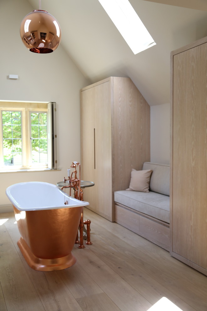 Cette photo montre une salle de bain principale tendance de taille moyenne avec un placard à porte plane, des portes de placard beiges, une baignoire indépendante, un mur blanc, parquet clair et un sol beige.