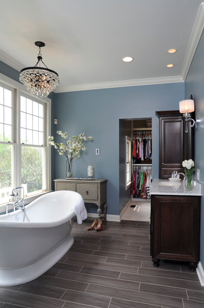 Imagen de cuarto de baño clásico con bañera exenta, armarios con paneles empotrados, puertas de armario de madera en tonos medios, suelo marrón y vestidor