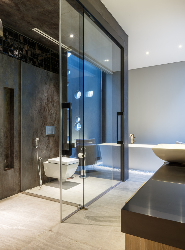 Foto på ett funkis badrum, med ett fristående badkar, en kantlös dusch, en vägghängd toalettstol, grå väggar, ett fristående handfat och dusch med skjutdörr