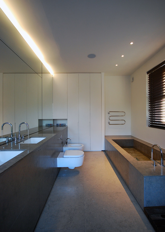 ロンドンにある高級な広いコンテンポラリースタイルのおしゃれなマスターバスルーム (一体型シンク、フラットパネル扉のキャビネット、白いキャビネット、ライムストーンの洗面台、ドロップイン型浴槽、オープン型シャワー、壁掛け式トイレ、茶色いタイル、石スラブタイル、白い壁、ライムストーンの床) の写真