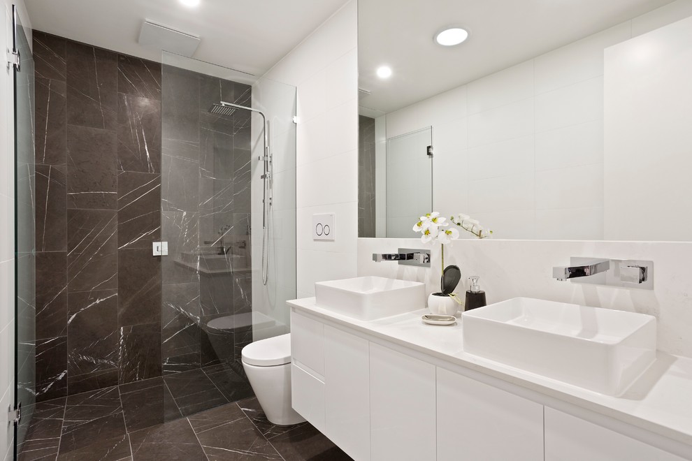 Cette photo montre une salle de bain tendance avec un placard à porte plane, des portes de placard blanches, une douche à l'italienne, un carrelage gris, un mur blanc, une vasque, un sol gris, une cabine de douche à porte battante et un plan de toilette blanc.
